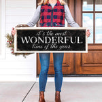 a woman holding a sign that says it's the most wonderful time of the