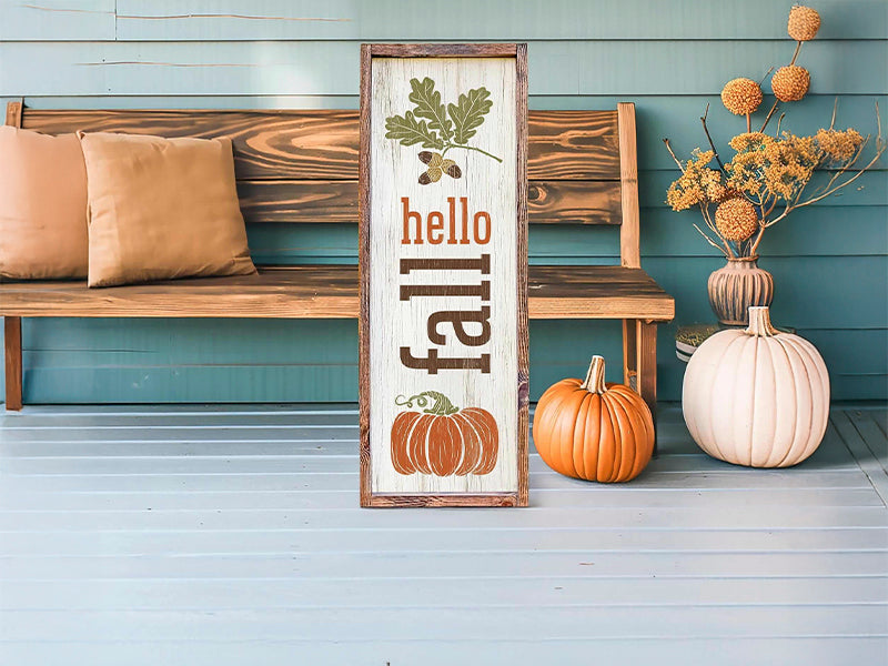 Hello fall sign with pumpkin, surrounded by autumn leaves and gourds on a porch.