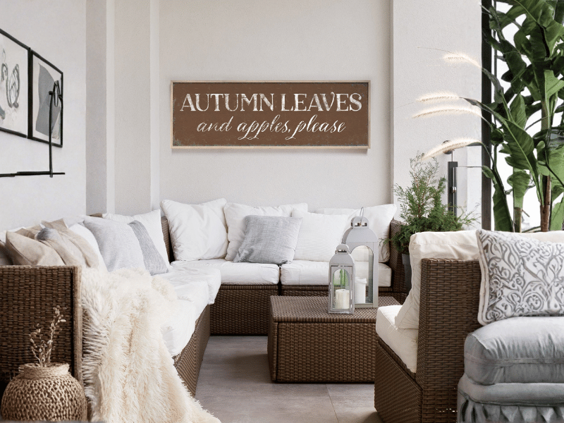Cozy patio with wicker furniture, cushions, plants, and a wall sign that reads "Autumn leaves and apples, please.