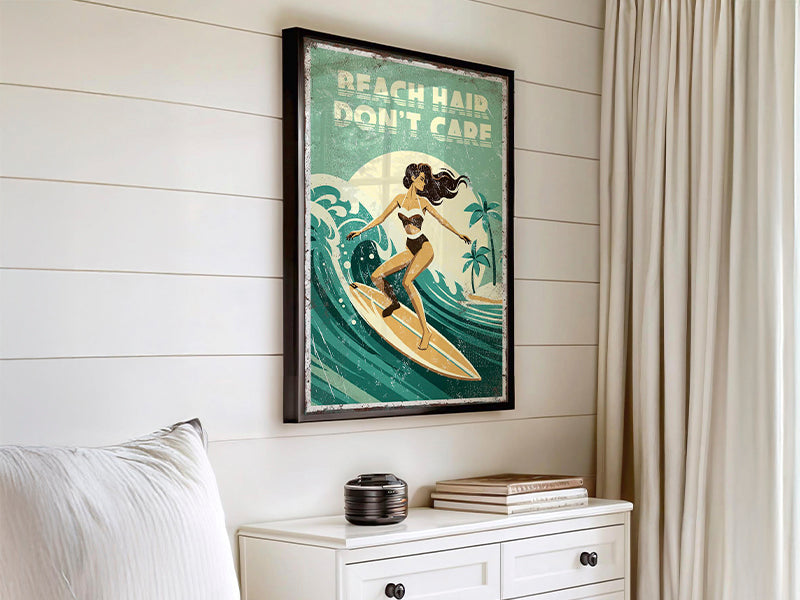 Framed surfing poster on wall in a bright bedroom above a white dresser and beside cream curtains.