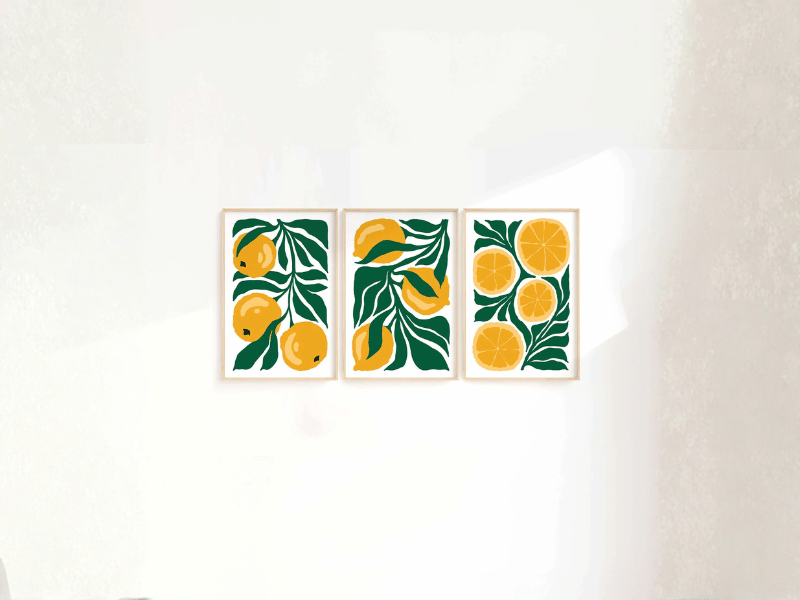 Three framed prints of yellow lemons and green leaves arranged on a white wall, sunlit from the right side.