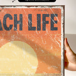 a person holding up a sign that says beach life