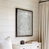 a framed sign with a list of rules for a lake house, hanging on a wall next to a white dresser.