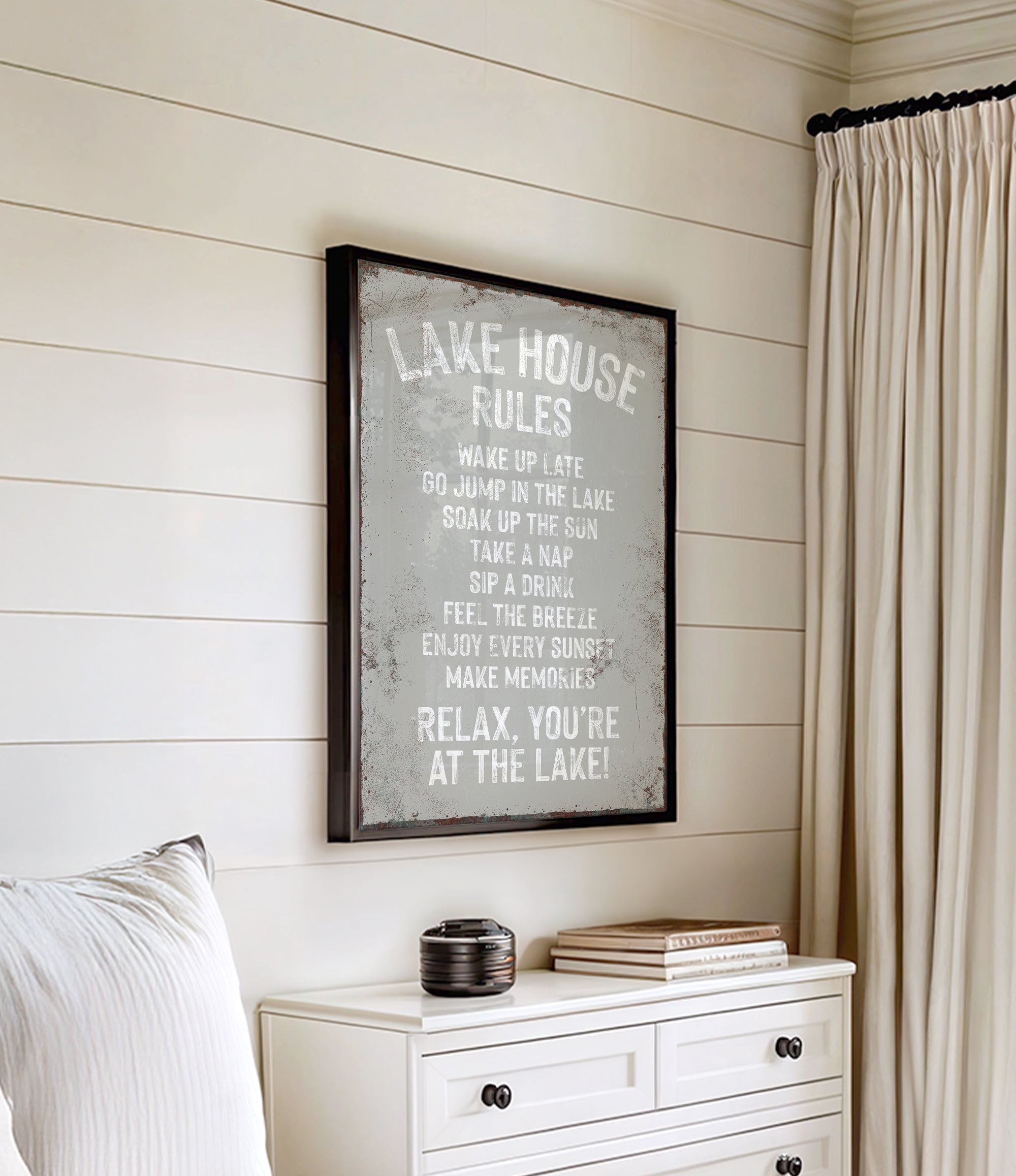 a framed sign with a list of rules for a lake house, hanging on a wall next to a white dresser.