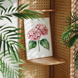 a framed painting of a pink hydrangea flower on a wooden shelf, surrounded by lush green leaves.