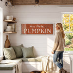 A woman stands in a cozy kitchen, gazing out a window at a pumpkin sign that reads "hey there, PUMPKIN".