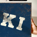 a hand holding a blue canvas print with a large white letter "K" on it.