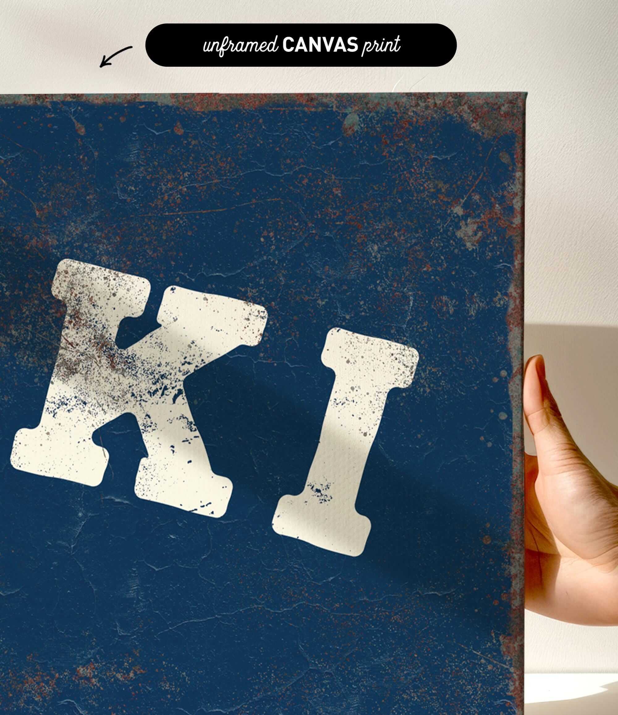 a hand holding a blue canvas print with a large white letter "K" on it.