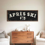 a wooden dresser with a sign above it that says "APRÈS SKI", and there are two white chairs and a vase with flowers on the dresser.