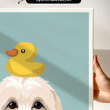 A hand is holding a framed print featuring a cartoon image of a duck sitting on a dog's head.