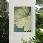 a large, vibrant green leaf with intricate patterns, hanging on a white wall. The leaf is framed in a wooden frame and is the central focus of the image.