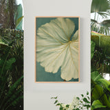 a large, vibrant green leaf with intricate patterns, hanging on a white wall. The leaf is framed in a wooden frame and is the central focus of the image.