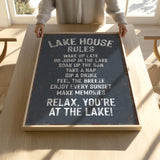 A person is holding up a sign that says "LAKESHOUSE RULES" on a wooden table.