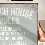 a hand holding a sign that says beach house rules