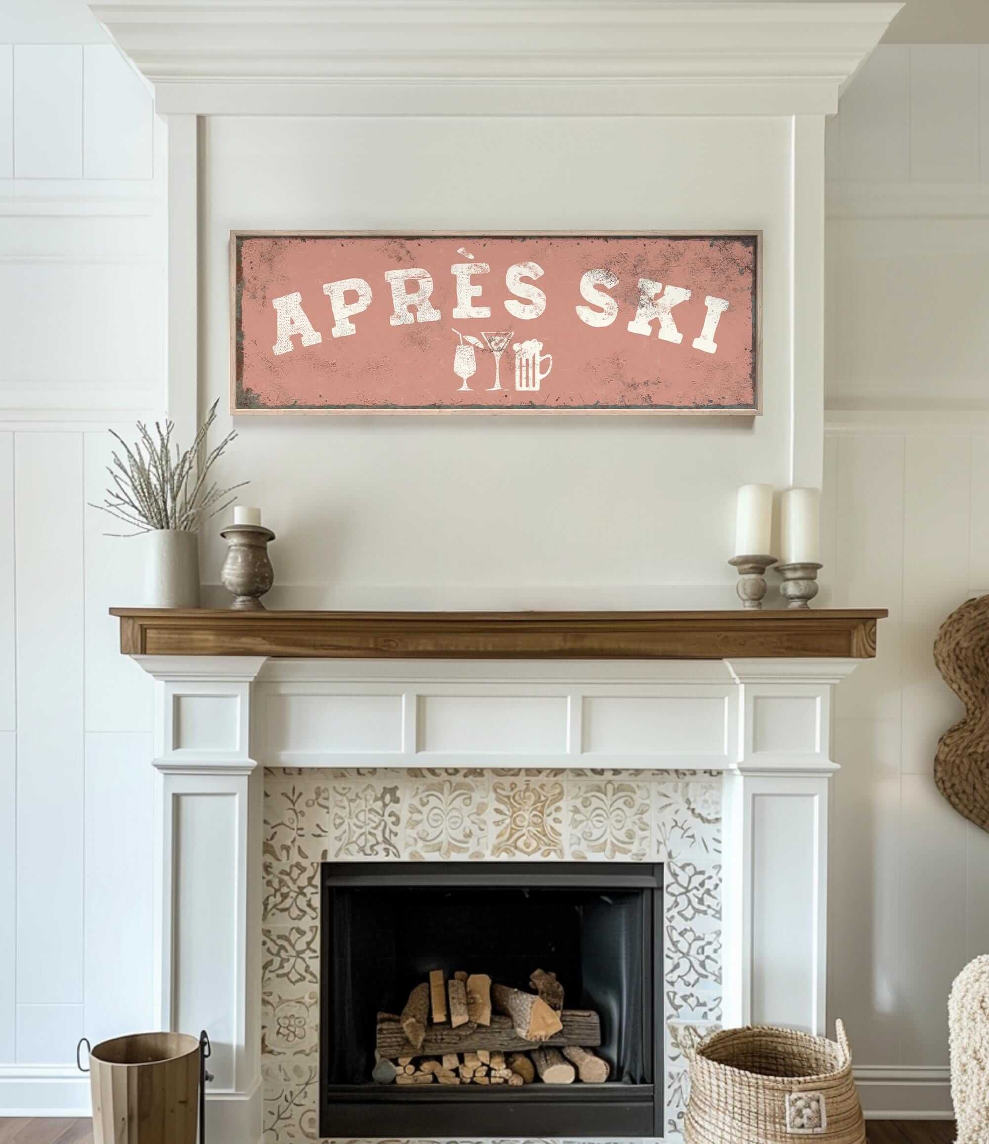 a cozy living room with a fireplace, a wooden mantel, and a framed sign that reads "APRÈS SKI". The mantel has a vase and a candle on it, adding to the warm and inviting atmosphere of the room.