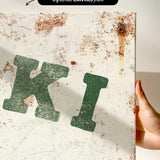 a close-up view of a white canvas print with a green and black text design. The text appears to be a stylized representation of the letters "K" and "I".