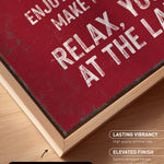 The image is a close-up of a maroon-colored canvas print with white text, placed on a wooden surface.