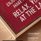 The image is a close-up of a maroon-colored canvas print with white text, placed on a wooden surface.