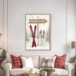 a cozy living room with a white sofa adorned with red and white plaid throw pillows. Above the sofa, there is a framed picture of a ski sign with the word "APRES" written on it. The room also includes a coffee table with a tray and a few decorative items, creating a warm and inviting atmosphere.