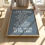 A person is holding up a sign that says "LAKESHOUSE RULES" in a wooden frame.