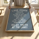 A person is holding up a sign that says "LAKESHOUSE RULES" in a wooden frame.