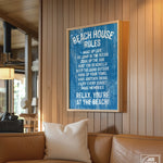 The Beach House Rules Sign, Painted Wood, Ocean Blue, adds charming coastal wall art to a cozy, sunlit living room with a tan couch and wooden walls.