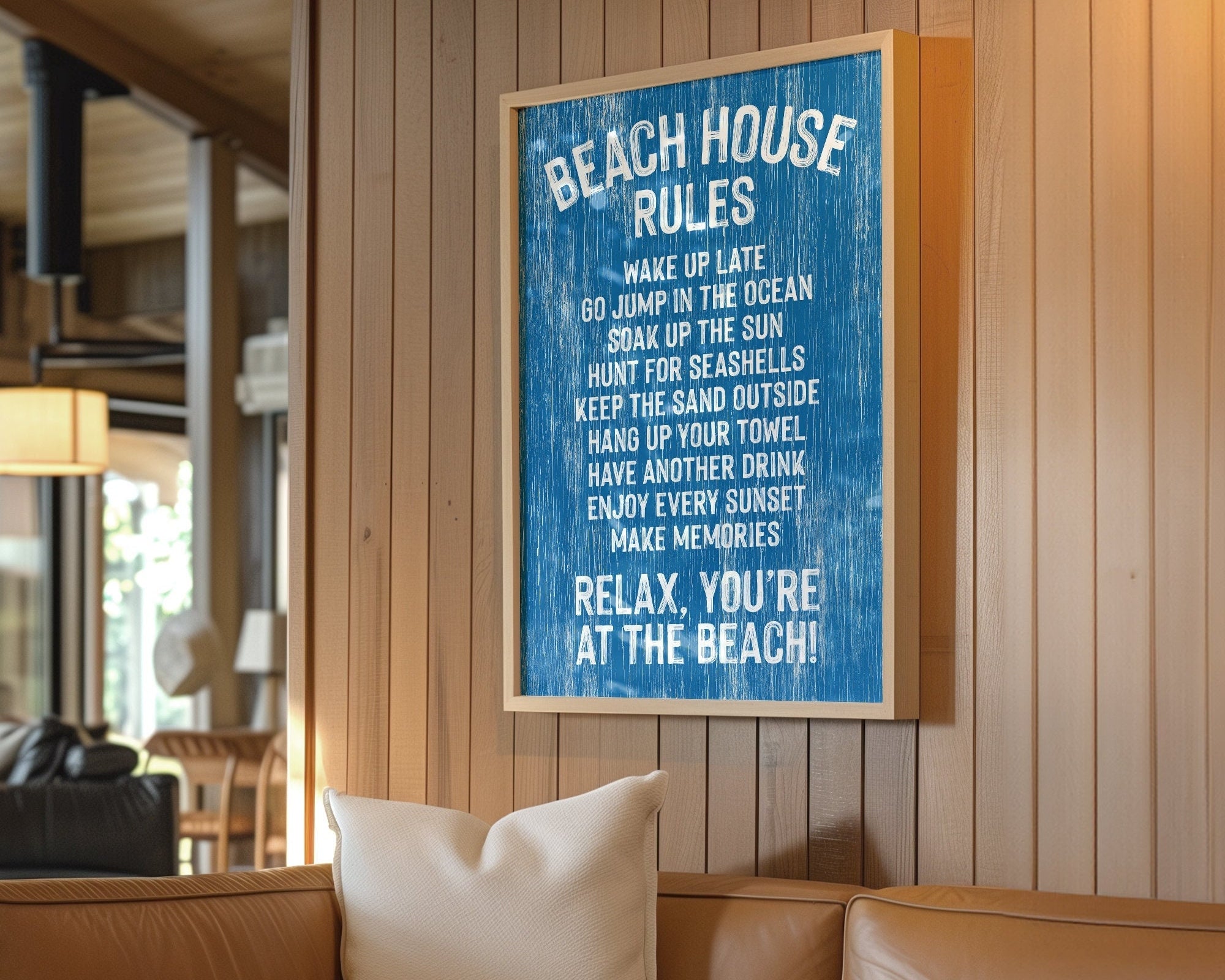 The Beach House Rules Sign, Painted Wood, Ocean Blue, adds charming coastal wall art to a cozy, sunlit living room with a tan couch and wooden walls.