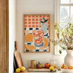 a kitchen counter with a framed painting of a glass of orange juice, a vase of flowers, and various fruits and vegetables such as oranges, lemons, and a pumpkin.
