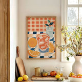 a kitchen counter with a framed painting of a glass of orange juice, a vase of flowers, and various fruits and vegetables such as oranges, lemons, and a pumpkin.