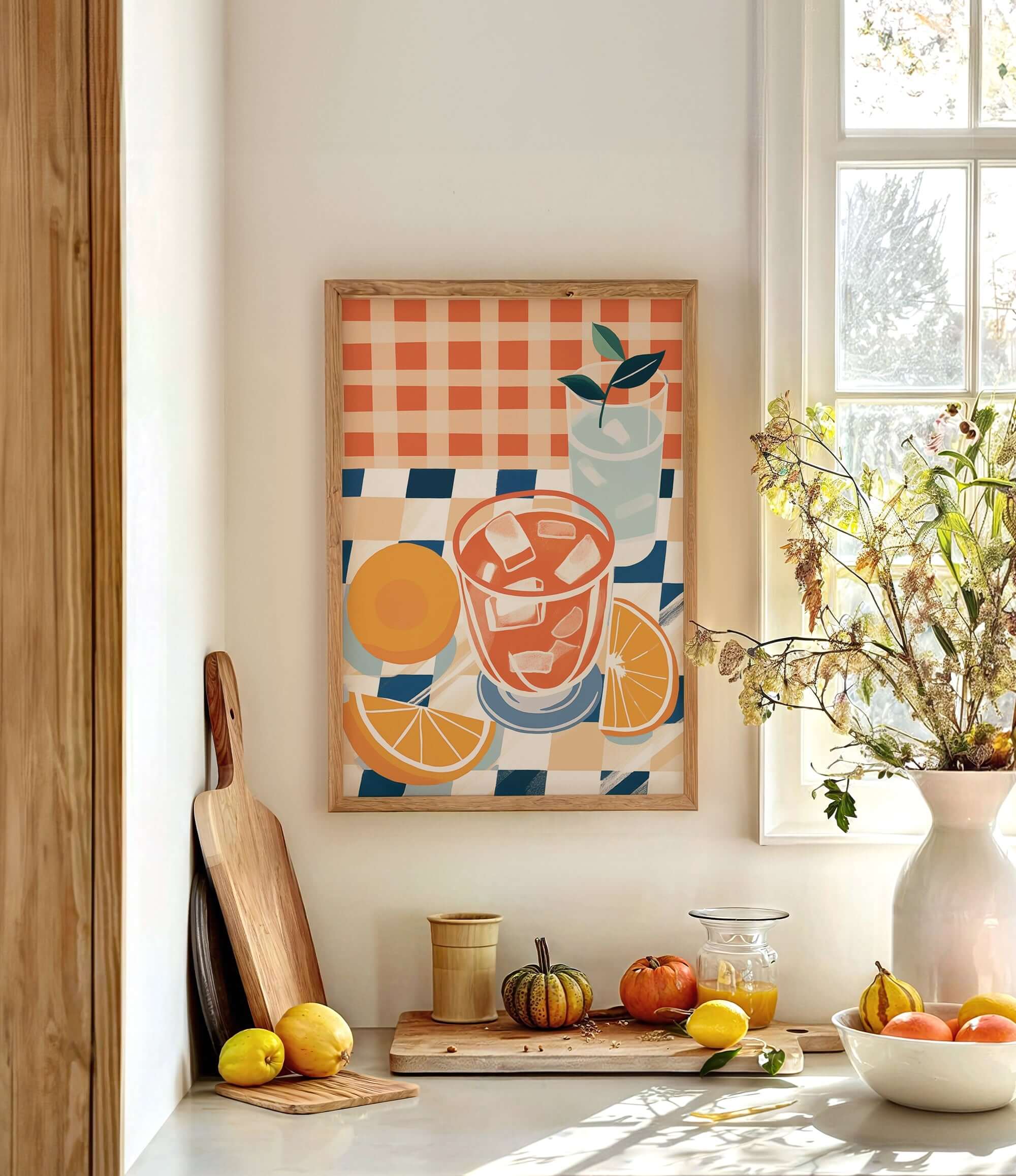 a kitchen counter with a framed painting of a glass of orange juice, a vase of flowers, and various fruits and vegetables such as oranges, lemons, and a pumpkin.