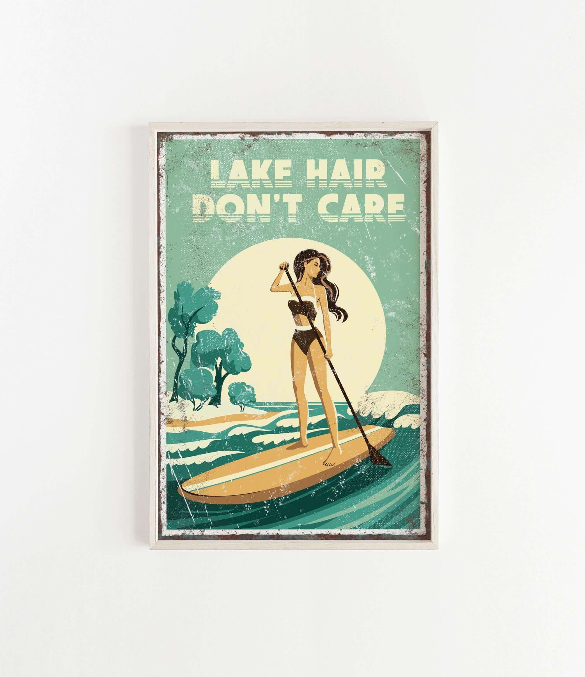 The image is a framed poster with a vintage-style illustration of a woman paddleboarding on a lake. The poster features the text "LAKESHAIR DON'T CARE" prominently displayed.