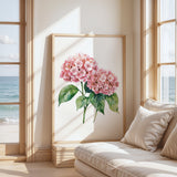 a large framed painting of pink hydrangeas on a wall, with a view of the ocean through a window in the background.