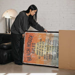 A woman is standing next to a large framed poster with text on it, which appears to be a beach house rules poster.