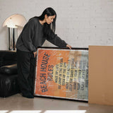 A woman is standing next to a large framed poster with text on it, which appears to be a beach house rules poster.