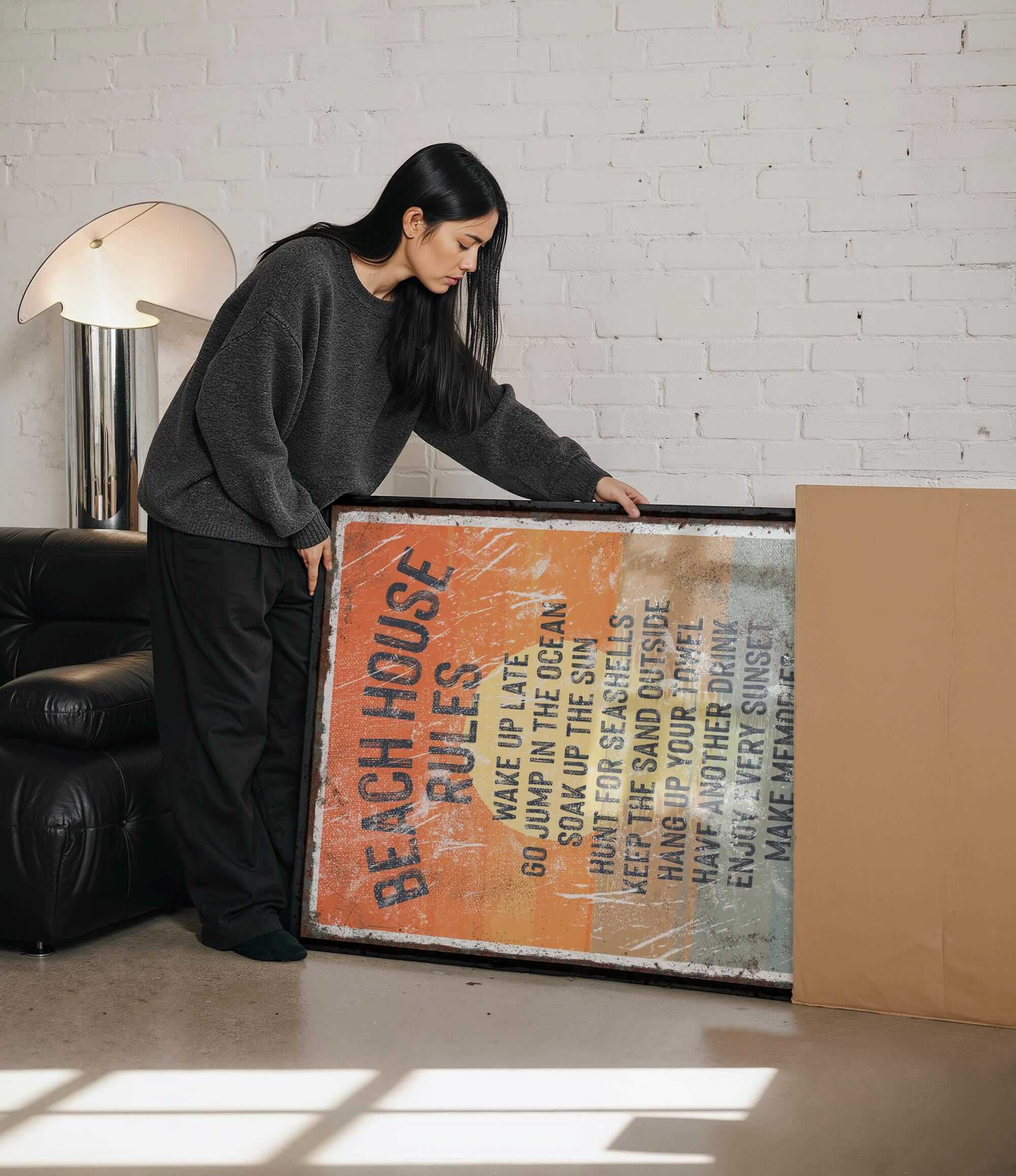 A woman is standing next to a large framed poster with text on it, which appears to be a beach house rules poster.