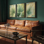 a living room with a brown leather couch, a wooden coffee table, and three framed prints of green leaves on the wall.