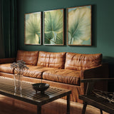 a living room with a brown leather couch, a wooden coffee table, and three framed prints of green leaves on the wall.