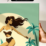 a hand holding a framed canvas print of a stylized illustration of a woman in a swimsuit, with palm trees and a sunset in the background.