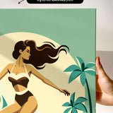 a hand holding a framed canvas print of a stylized illustration of a woman in a swimsuit, with palm trees and a sunset in the background.
