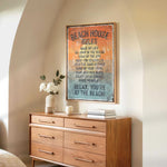 a wooden dresser with a framed sign that reads "BEACH HOUSE RULES" hanging on the wall above it. The dresser has a vase of white flowers and a stack of books on top.
