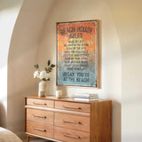 a wooden dresser with a framed sign that reads "BEACH HOUSE RULES" hanging on the wall above it. The dresser has a vase of white flowers and a stack of books on top.