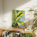 a wooden shelf with a framed painting of a banana tree, a lamp, and various books and plants.
