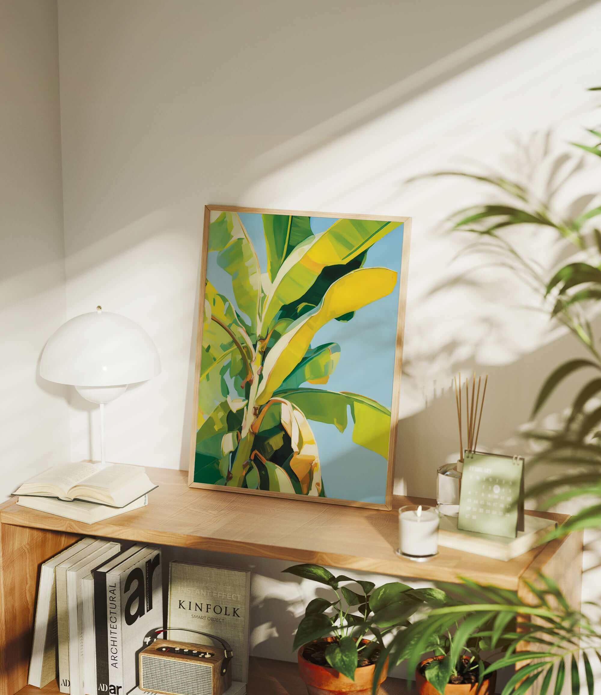 a wooden shelf with a framed painting of a banana tree, a lamp, and various books and plants.
