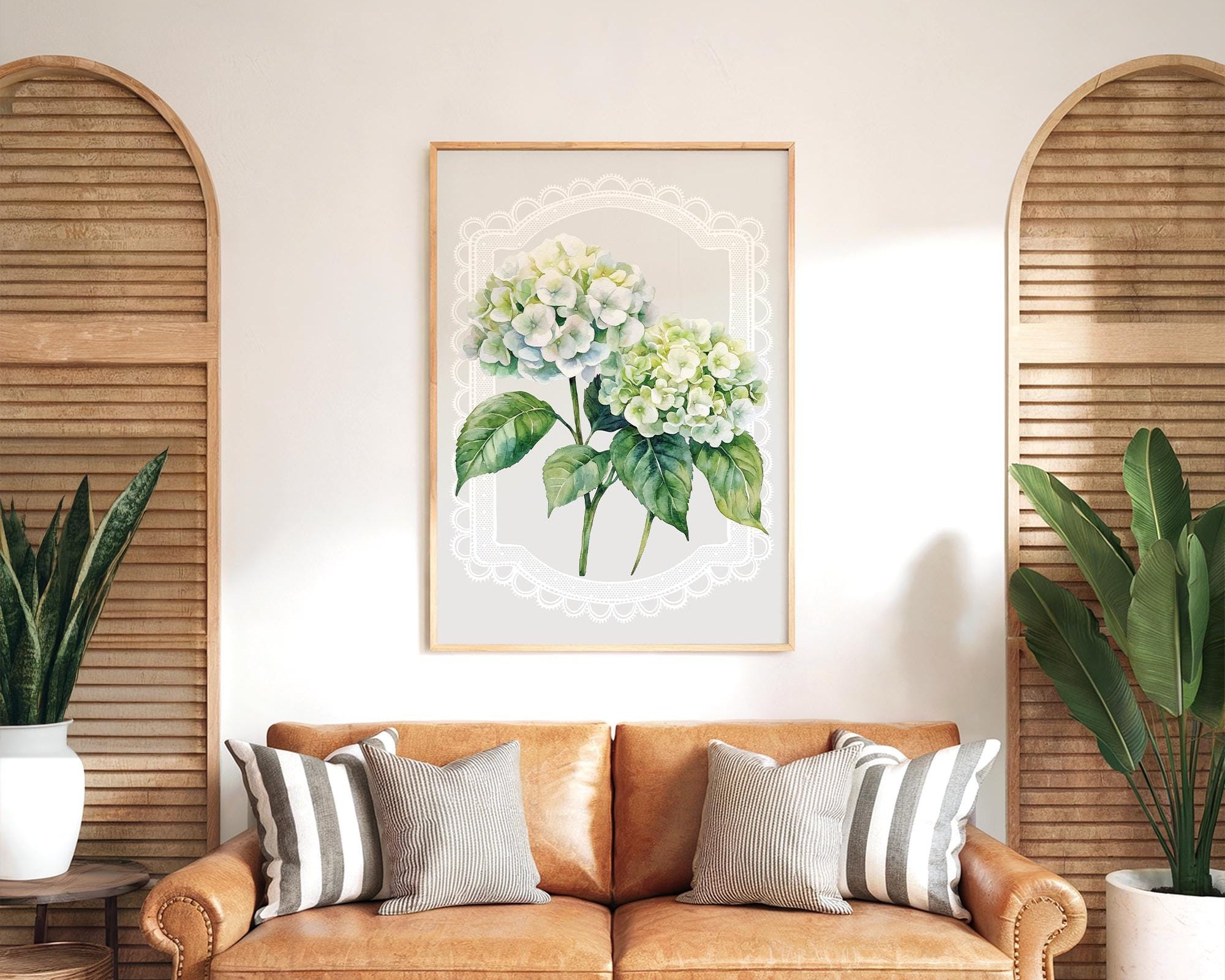 a cozy living room with a brown leather sofa adorned with striped pillows, a framed floral print hanging on the wall, and two potted plants on either side of the sofa.