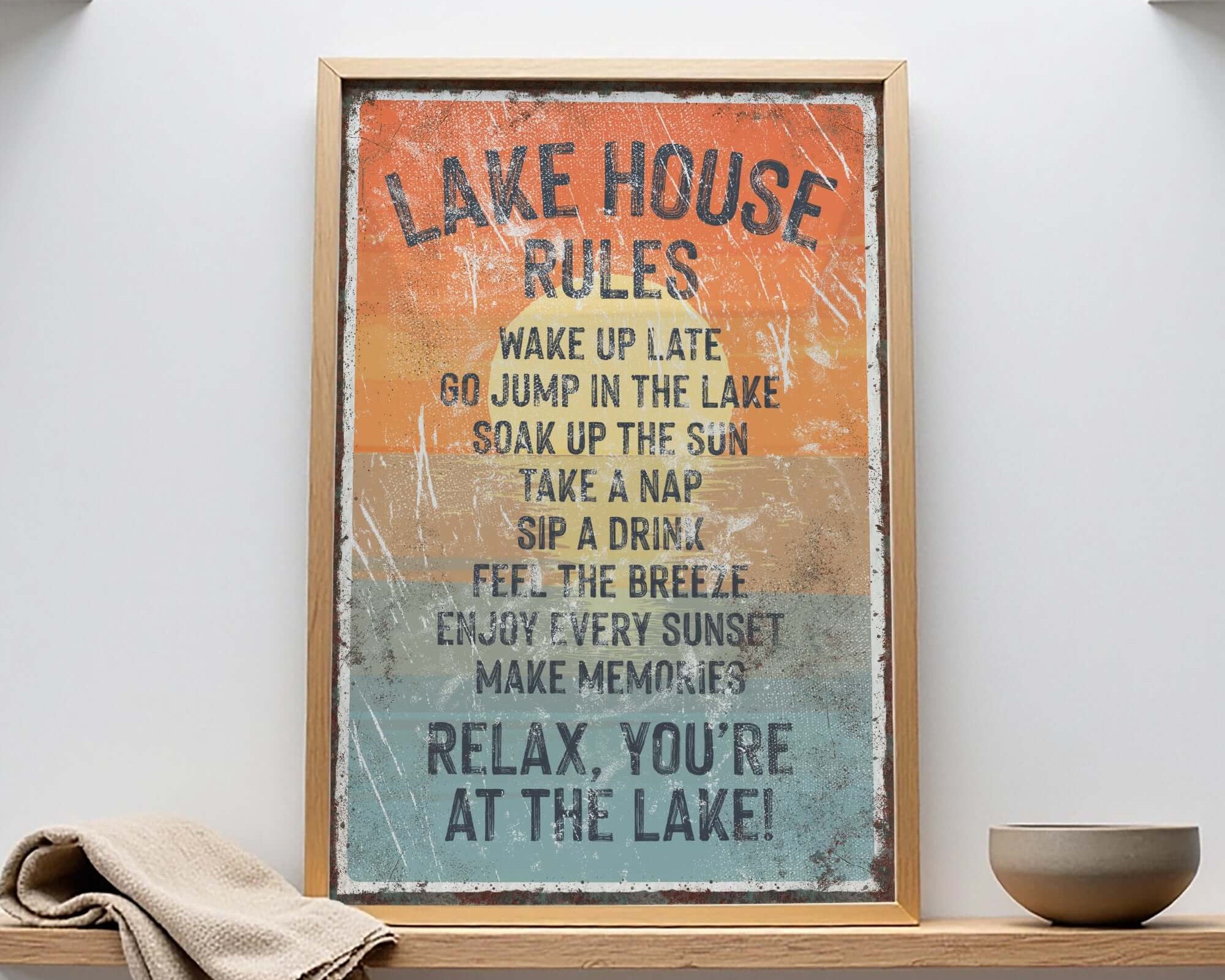 A framed sign with a list of rules for a lake house, including activities such as waking up late, jumping in the lake, taking a nap, drinking, taking a nap, drinking, feeling the breeze, enjoying the sunset, and making memories.