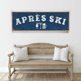 a wooden bench with two striped pillows, and above it is a framed sign with the text "APRÈS SKI" in white letters.