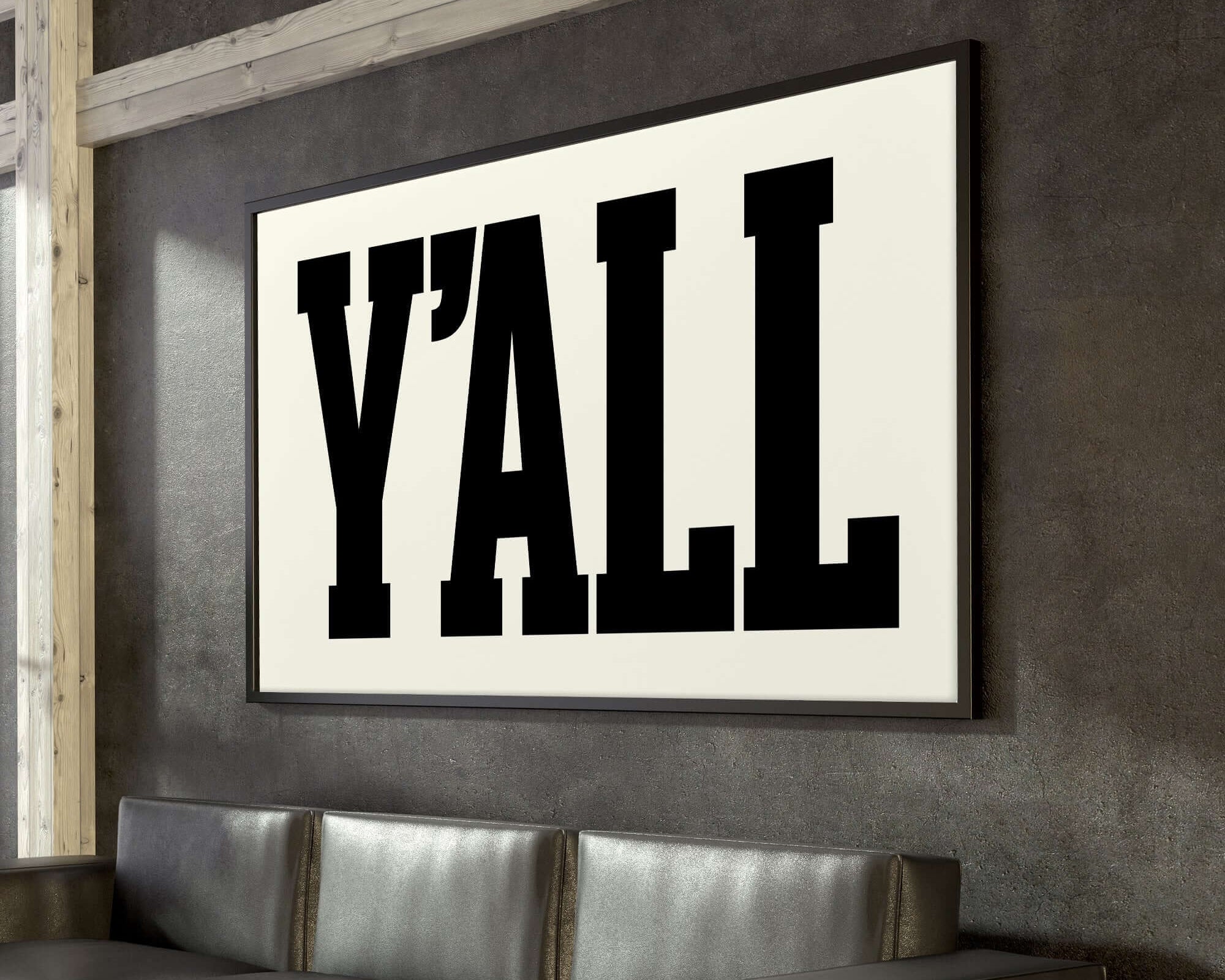 An off-white Y'all Sign Print hangs above a black leather couch, featuring bold black letters and bringing a modern farmhouse style to your home decor.