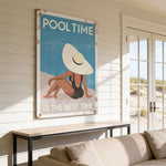 a large poster with a beach scene and a woman wearing a hat, hanging on a wall in a room with a couch and a window.