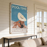 a large poster with a beach scene and a woman wearing a hat, hanging on a wall in a room with a couch and a window.