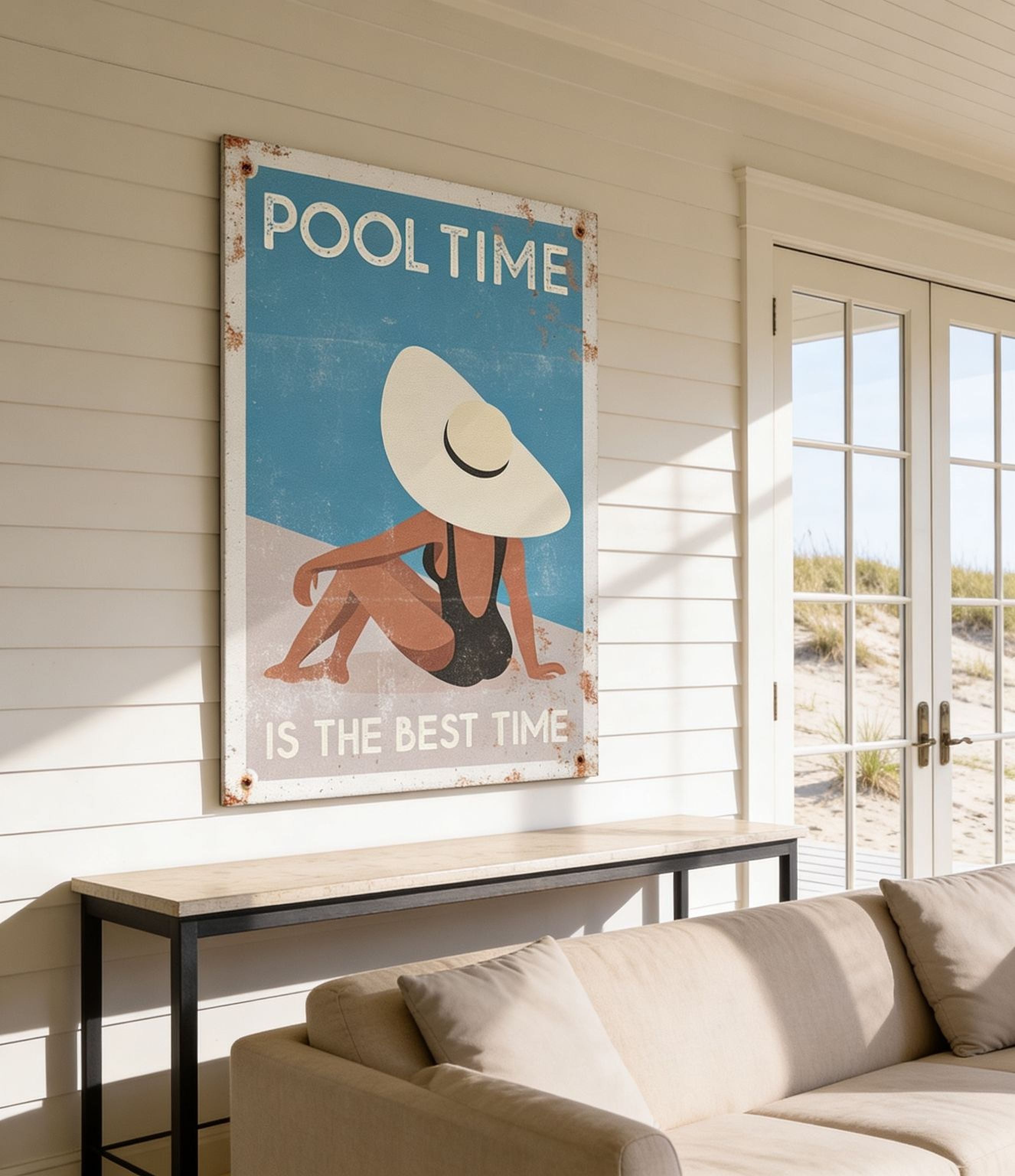 a large poster with a beach scene and a woman wearing a hat, hanging on a wall in a room with a couch and a window.